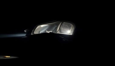An extreme close-up photograph of a damaged car part or piece of physical evidence from the crime scene, lit by a harsh, direct camera flash against a pitch-black background, capturing the stark, gritty, investigative nature of the incident.