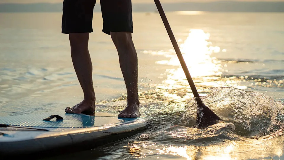 Male legs standing on paddleboard on water during sunset
