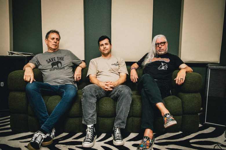 A wide shot of the three members of the band Down From Jersey sitting on a dark green couch in a recording studio.