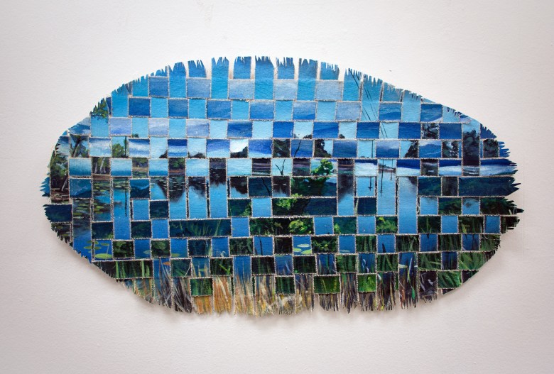 An oval-shaped mixed media artwork featuring a landscape scene of a lake and trees, created by weaving together strips of painted material.
