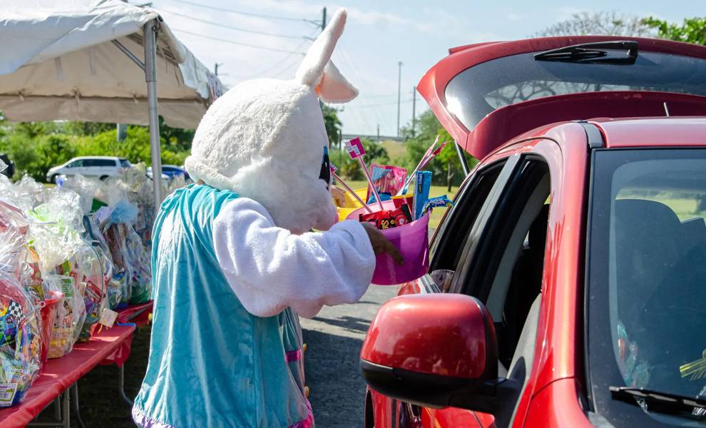 “Giving Thanks on Good Friday” brings hope and support to thousands across Miami-Dade 2 A person dressed in a white Easter bunny costume hands a pink basket filled with toys and treats through the window of a red car at a drive-through giveaway at Giving Thanks on Good Friday at The Caring Place.