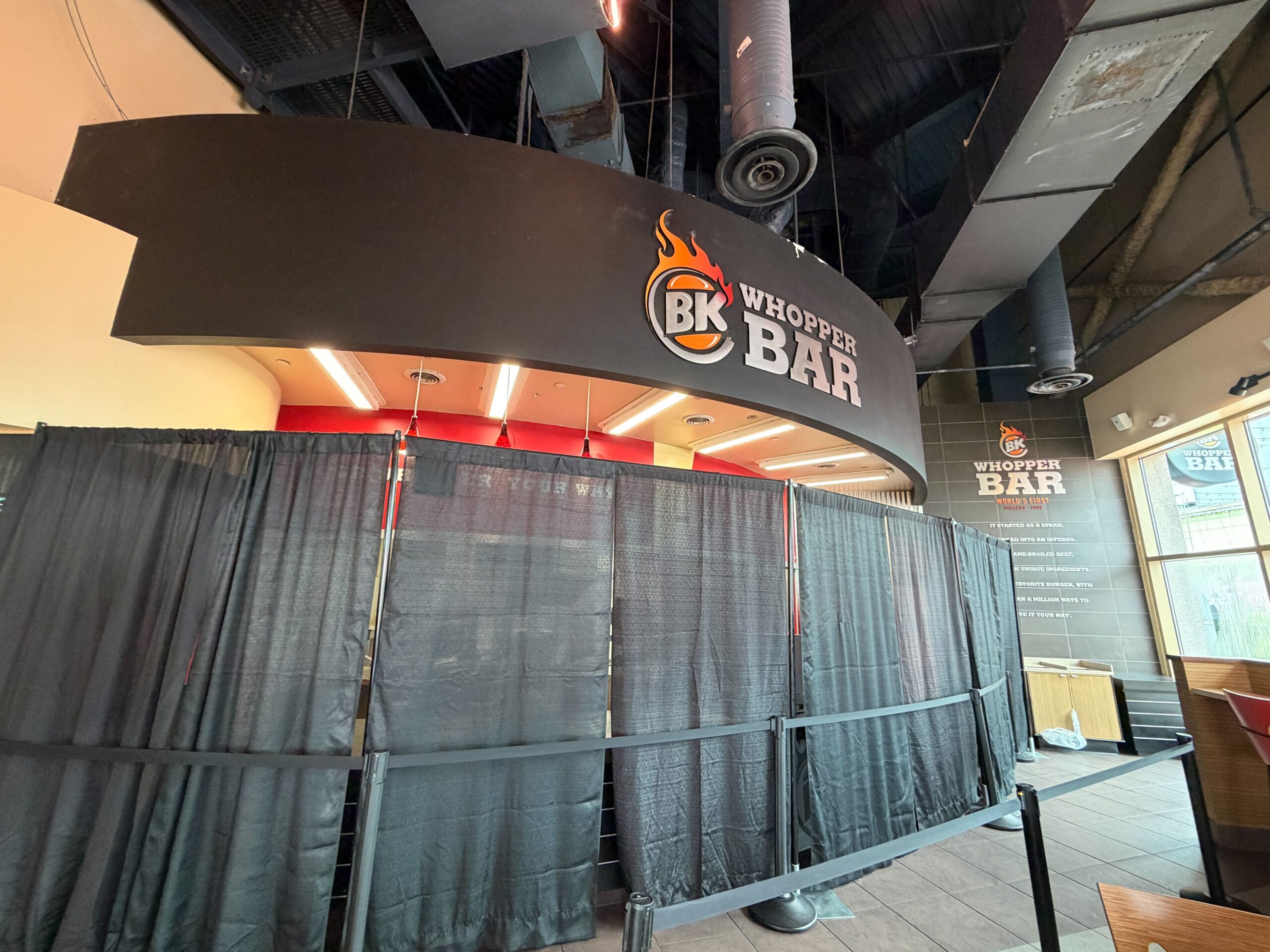 Inside, the Whopper Bar ordering area has been surrounded by privacy curtains and black scancions. We could see that the menus on the wall have been removed, though the rest of the restaurant's signage appears still intact.