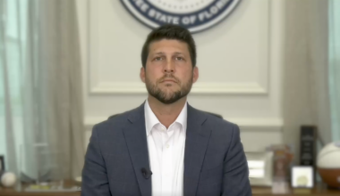 Florida Attorney General James Uthmeier speaks from his desk, donning a grey blazer and white shirt