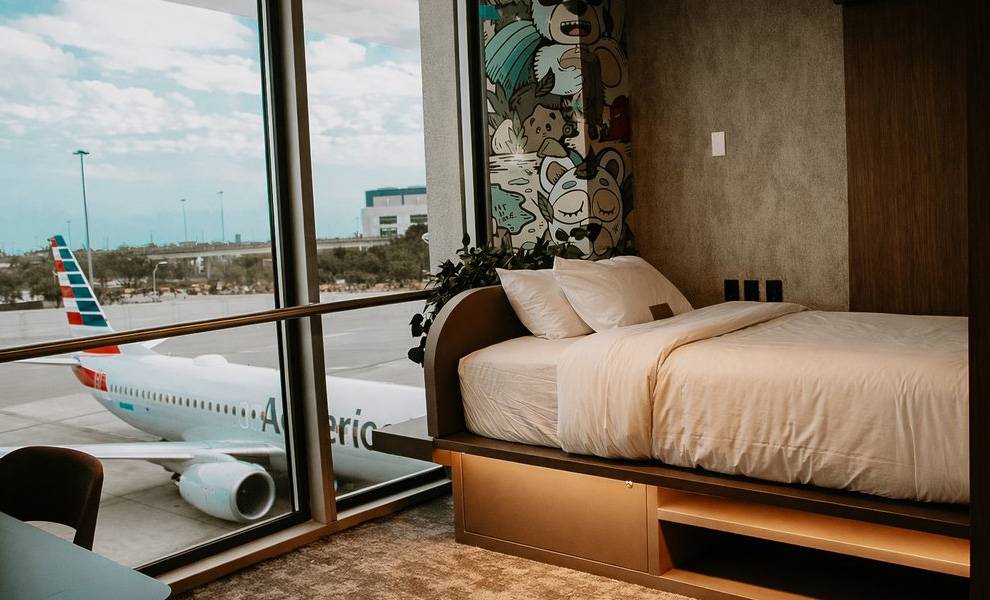 Miami International Airport debuts first-ever sleep rooms in North America 1 A modern airport hotel-style room at MIA features a neatly made bed positioned beside a large floor-to-ceiling window.