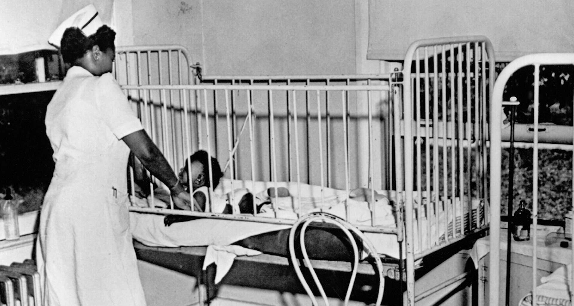 Black and white photo of a nurse standing over a crib in a hospital