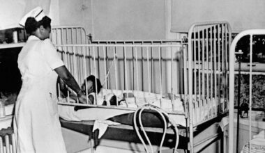 Black and white photo of a nurse standing over a crib in a hospital
