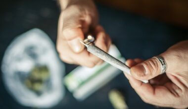 photo of a closeup of hands lighting a marijuana joint with marijuana on the table in a baggie on a table below