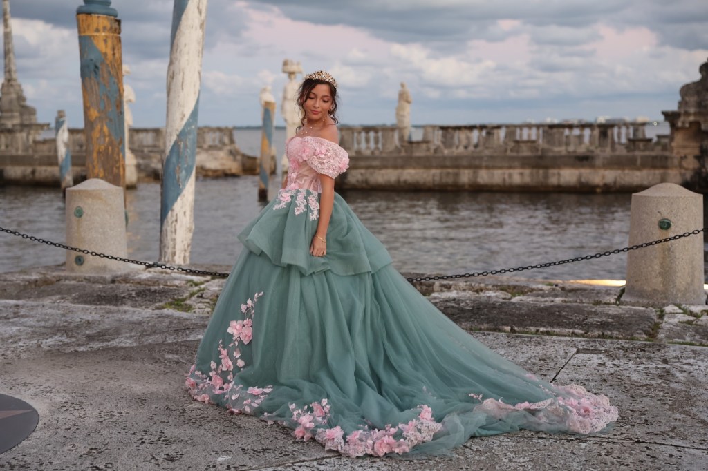 photo of a girl in a pink-and-teal quinceañera ballgown posing in front of a waterfront