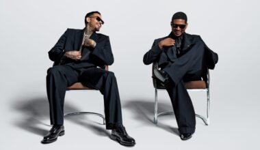 Photo of Usher and Chris Brown sitting on chairs wearing black suits.