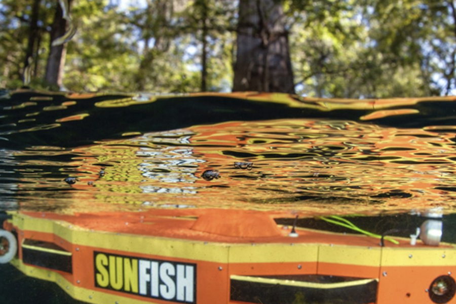 An orange and yellow underwater autonomous vehicle with the word "Sunfish" on its side sits just under the water.