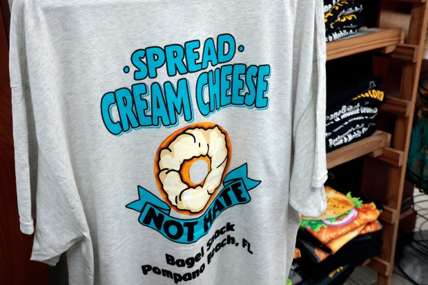 T-shirts with phrases like "Spread cream cheese, not hate," and "A bagel a day keeps the oy vey away," are for sale at Bagel Snack in Pompano Beach on Monday, April 6, 2026. The restaurant is the Best of South Florida Dining winner for best deli and also won best bagels in 2024. (Amy Beth Bennett / South Florida Sun Sentinel)