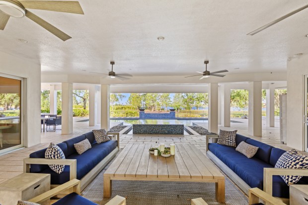 A covered lanai offers multiple lounge zones, a summer kitchen with a built-in grill and beverage refrigerator, ceiling fans, and an open-air shower, all positioned to maximize sunset views over the lake. (Photo courtesy of Pozek Group)