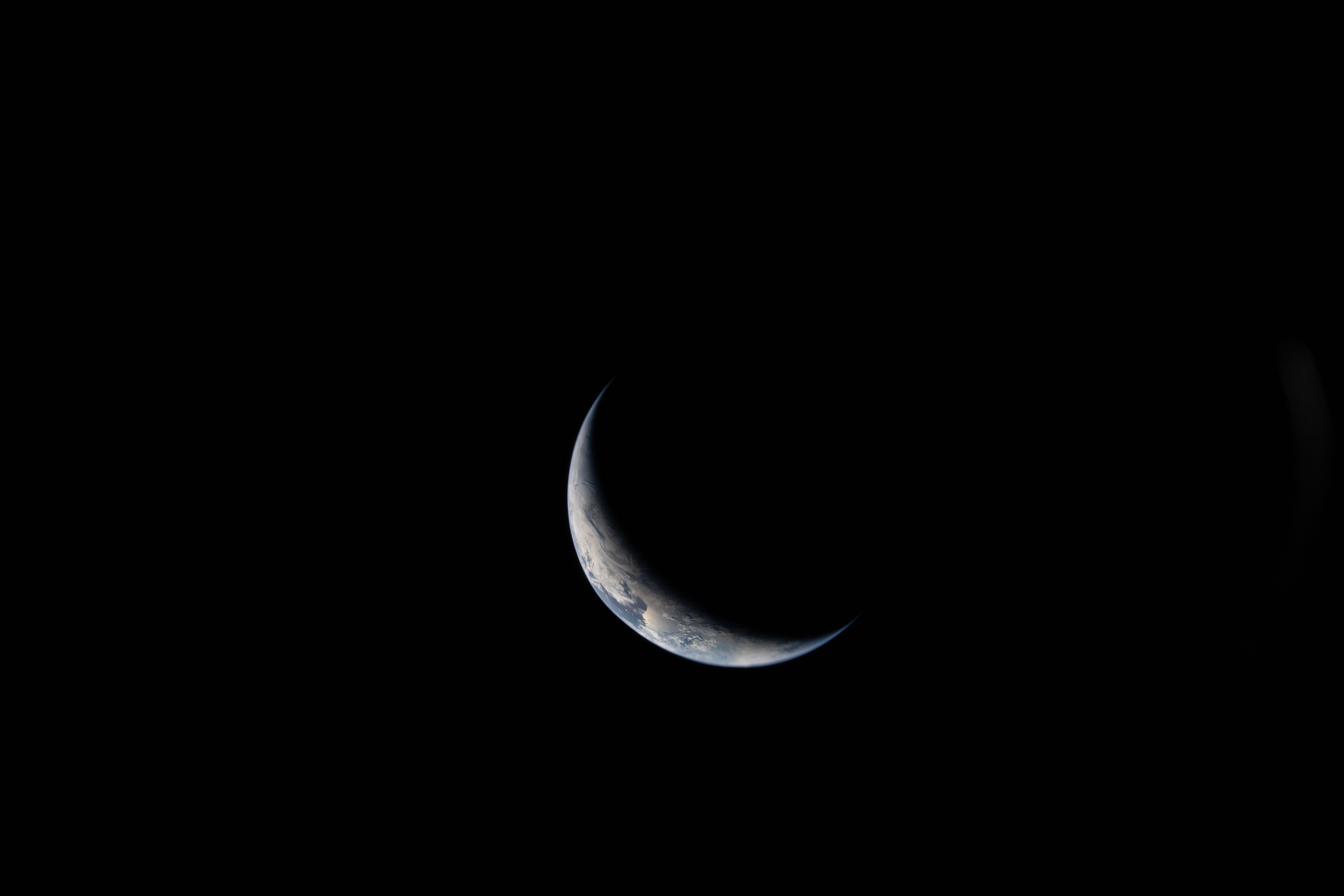 A sliver of Earth is illuminated against the blackness of...