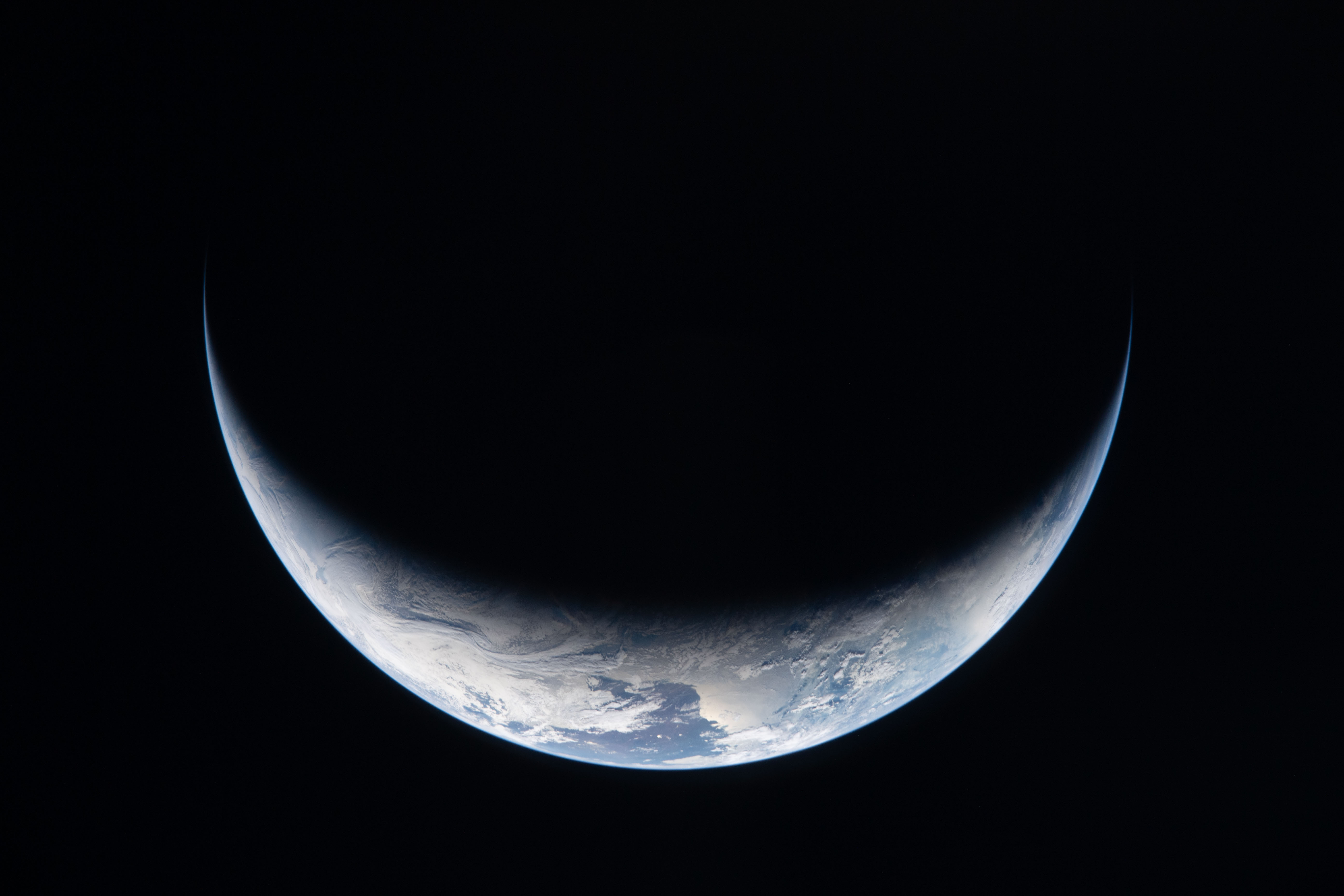 A sliver of Earth is illuminated against the blackness of...