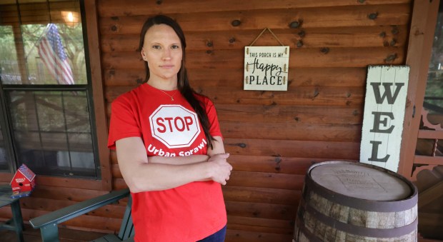Rachel Hildebrand, standing in front of her family home on Chuluota Road, wears a red "STOP Urban Sprawl" t-shirt identifying east Orange County residents opposed to urban-style development in their rural community. She is the last plaintiff standing in a statewide legal battle against a 2025 Florida law that curtails local communities' ability to control growth.ounty, at her rural home on Chuluota Road in east Orange County, Wednesday, April 8, 2026. Hildebrand is fighting plans for an 1,800-home development proposed for the cattle pastureland across from her home. (Joe Burbank/Orlando Sentinel)