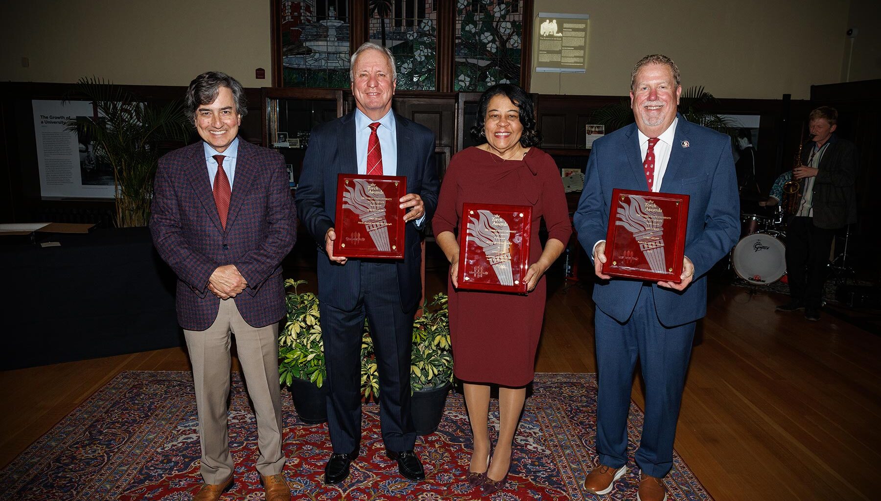 Three men in suits and a woman in a garnet dress hold plaques honoring them as Torch Award winners.