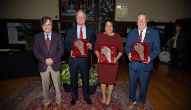 Three men in suits and a woman in a garnet dress hold plaques honoring them as Torch Award winners.