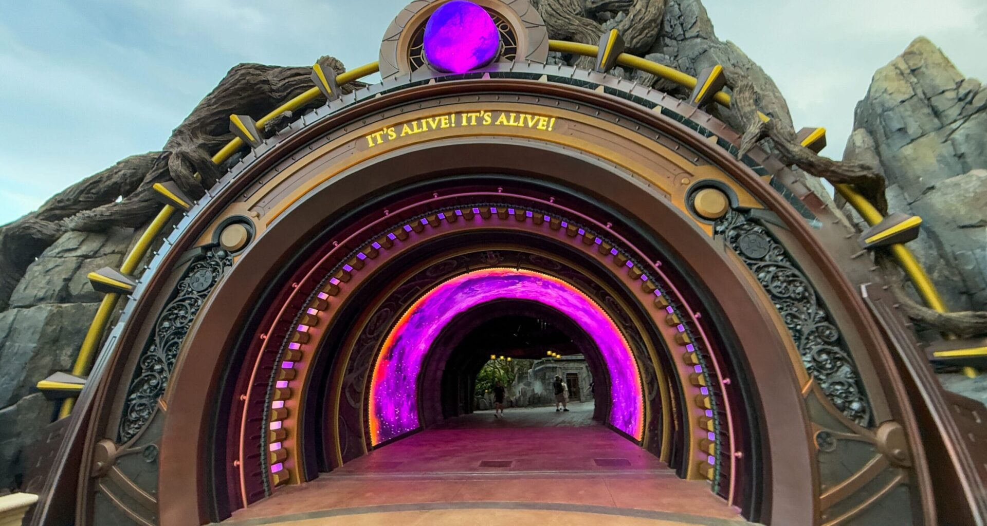 A large, decorative tunnel entrance with glowing purple lights welcomes guests into Epic Universe