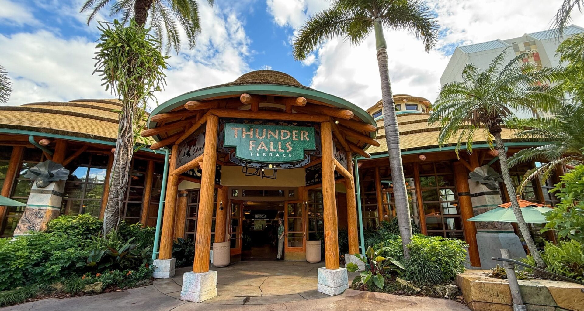 Entrance of Thunder Falls Terrace at Islands of Adventure, with palm trees and tropical-themed architecture under a blue sky.