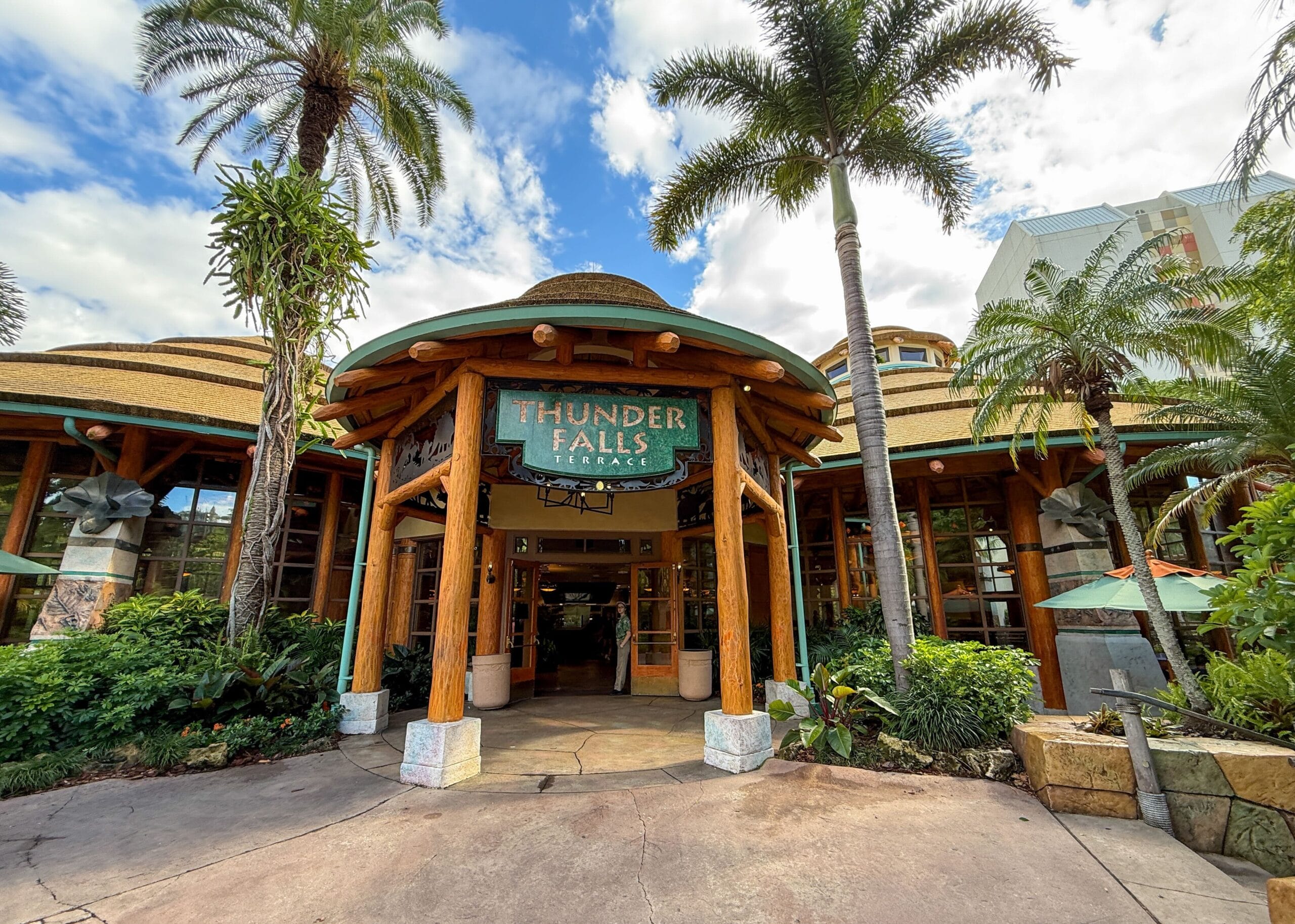 Entrance of Thunder Falls Terrace at Islands of Adventure, with palm trees and tropical-themed architecture under a blue sky.
