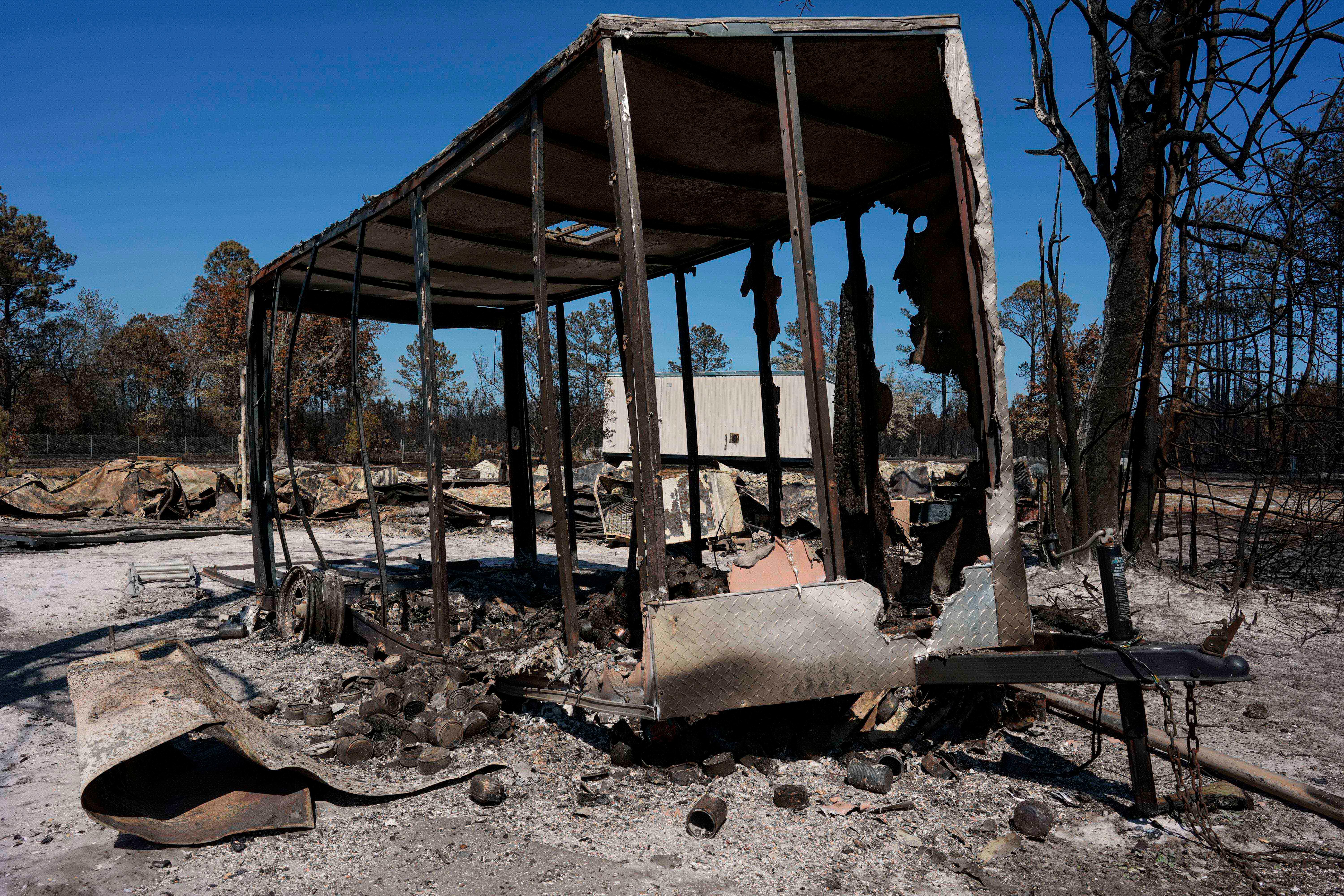A burned trailer sits near a destroyed home as the...