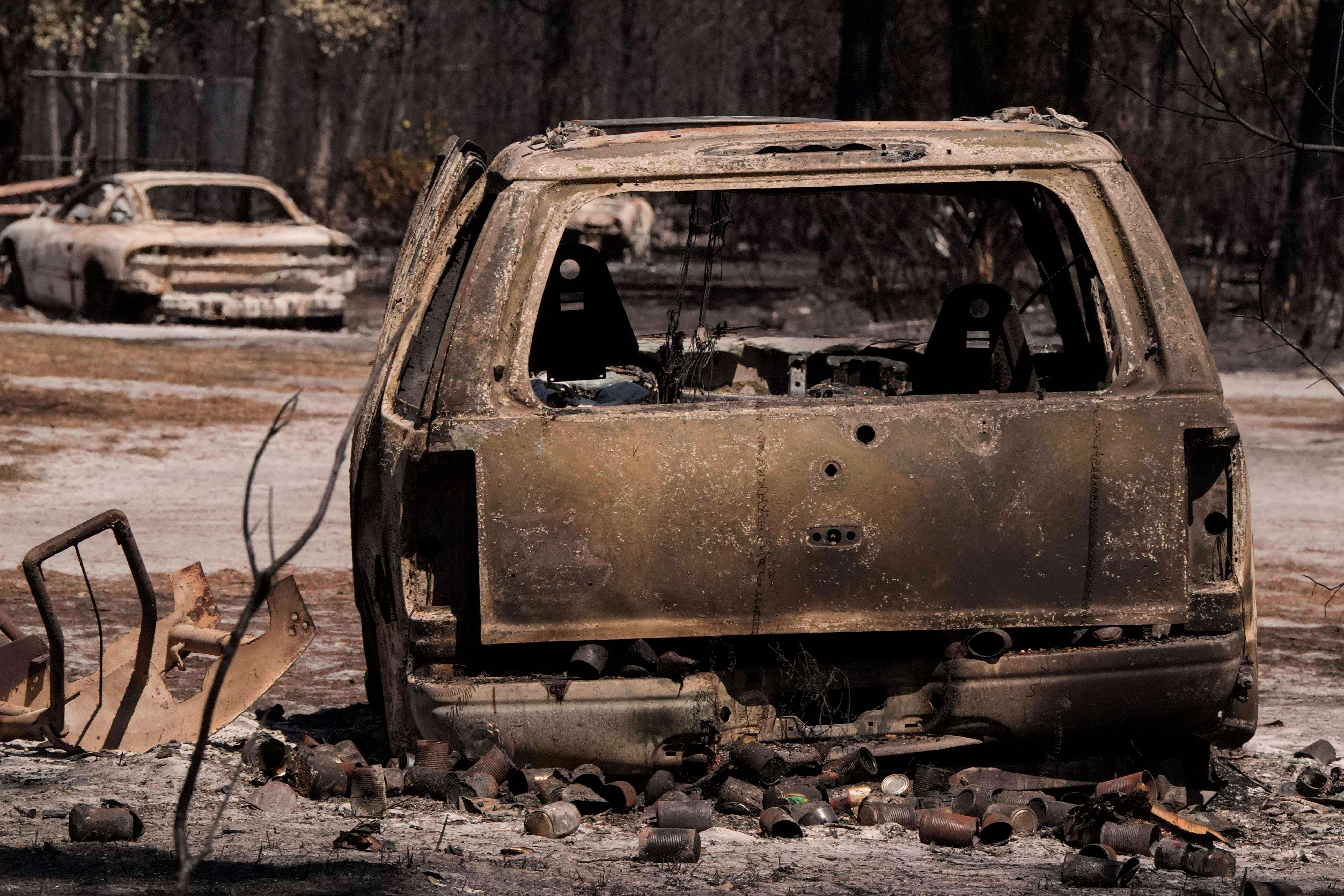 A burned vehicle sits near a destroyed home as the...