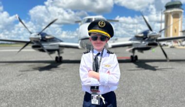 Child dressed as a pilot stands in front of an airplane on a runway