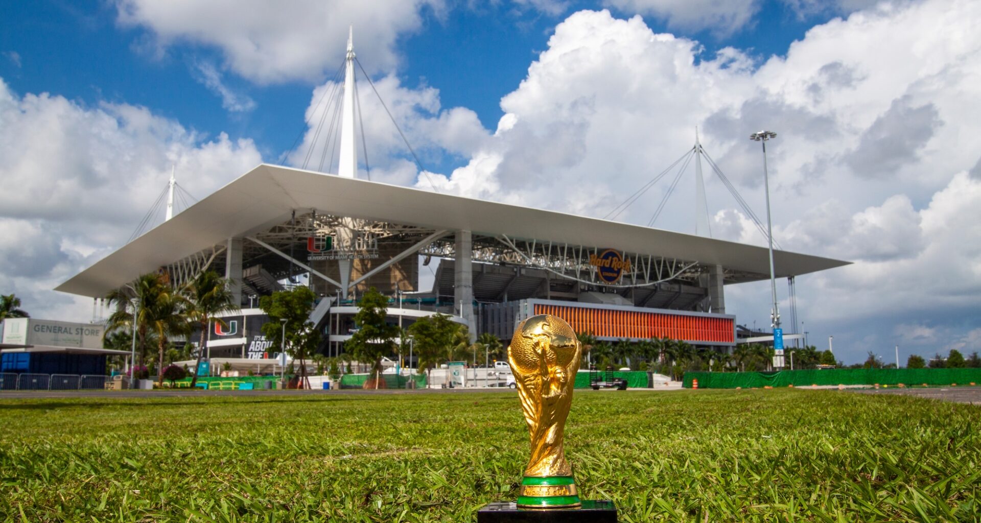 photo of the World Cup trophy on the grass in front of Miami's Hard Rock Stadium, which looms in the background