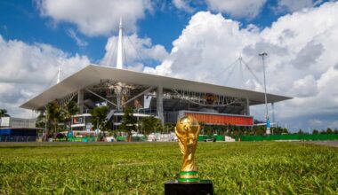 photo of the World Cup trophy on the grass in front of Miami's Hard Rock Stadium, which looms in the background