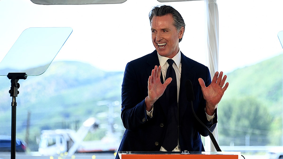 Governor Gavin Newsom speaking at a wooden podium outdoors in Agoura Hills, California