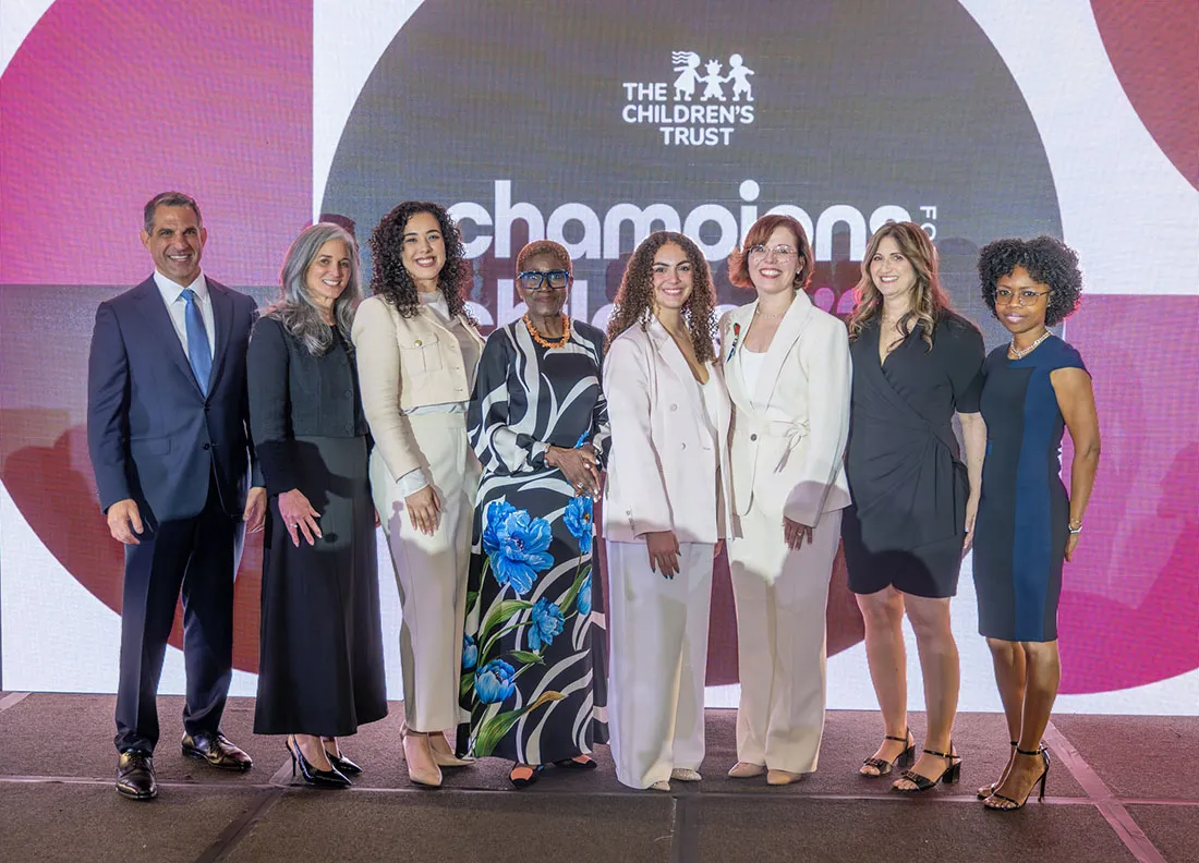 Group photo of award honorees and presenters standing on a stage at The Children’s Trust Champions for Children Awards 2026, with branded event signage and a large digital backdrop behind them.