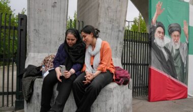 Women share a moment as they look at a smartphone at the main gate of the Tehran University as a banner shows portraits of the late Supreme Leader Ayatollah Ali Khamenei, right, and the late revolutionary founder Ayatollah Khomeini in Tehran, Iran, Sunday, April 19, 2026. (AP Photo/Vahid Salemi)