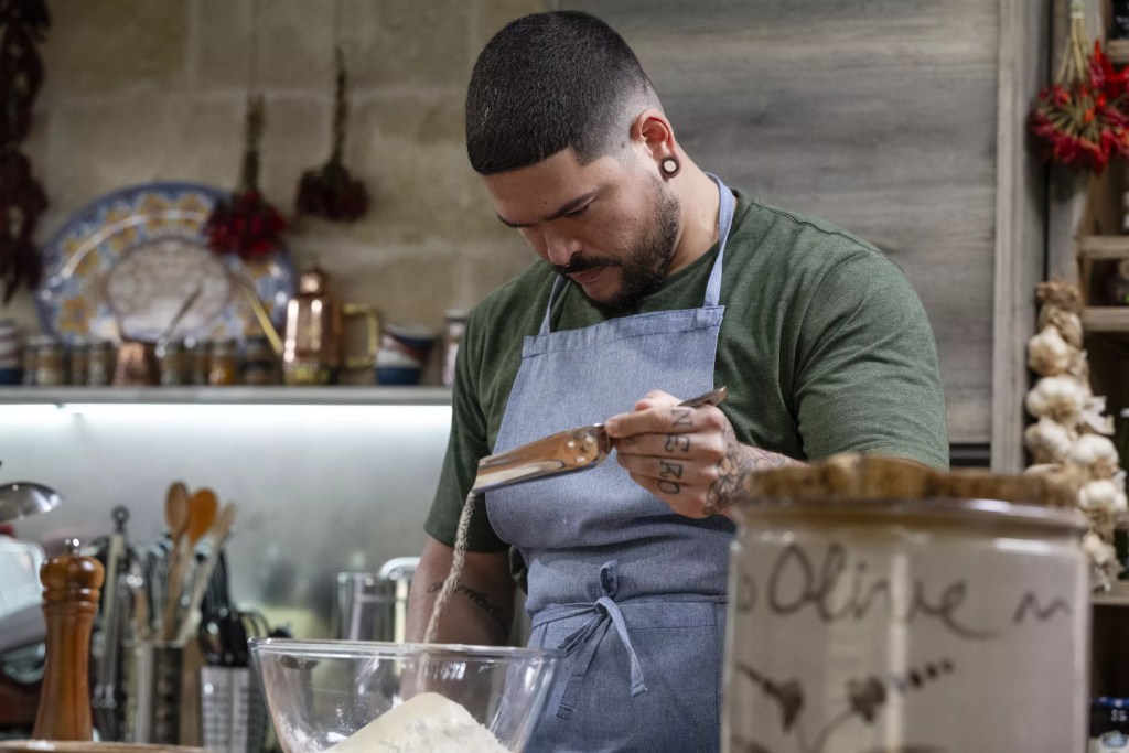 a man cooking in a green shirt and blue apron