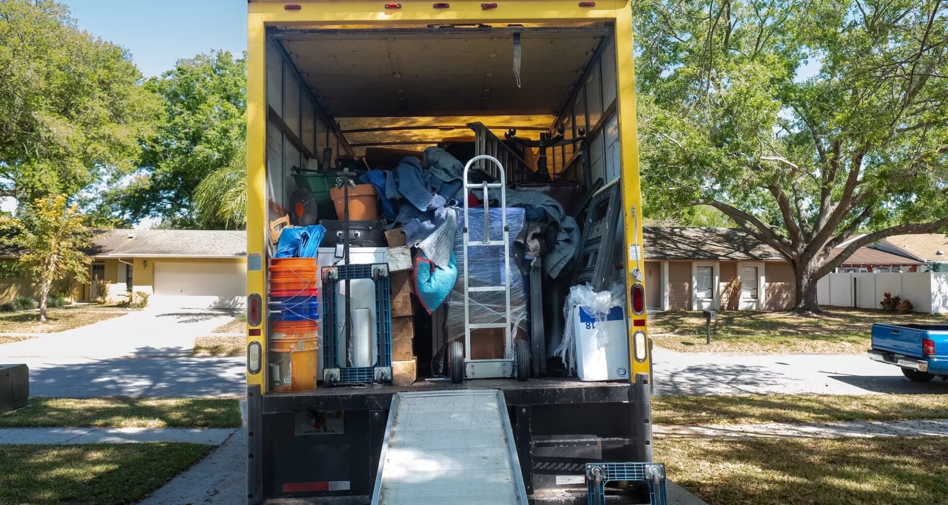 Belongings from a house loaded into a moving van, viewed from the back of the truck, including ramp and dolly.