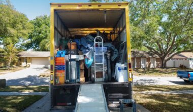 Belongings from a house loaded into a moving van, viewed from the back of the truck, including ramp and dolly.