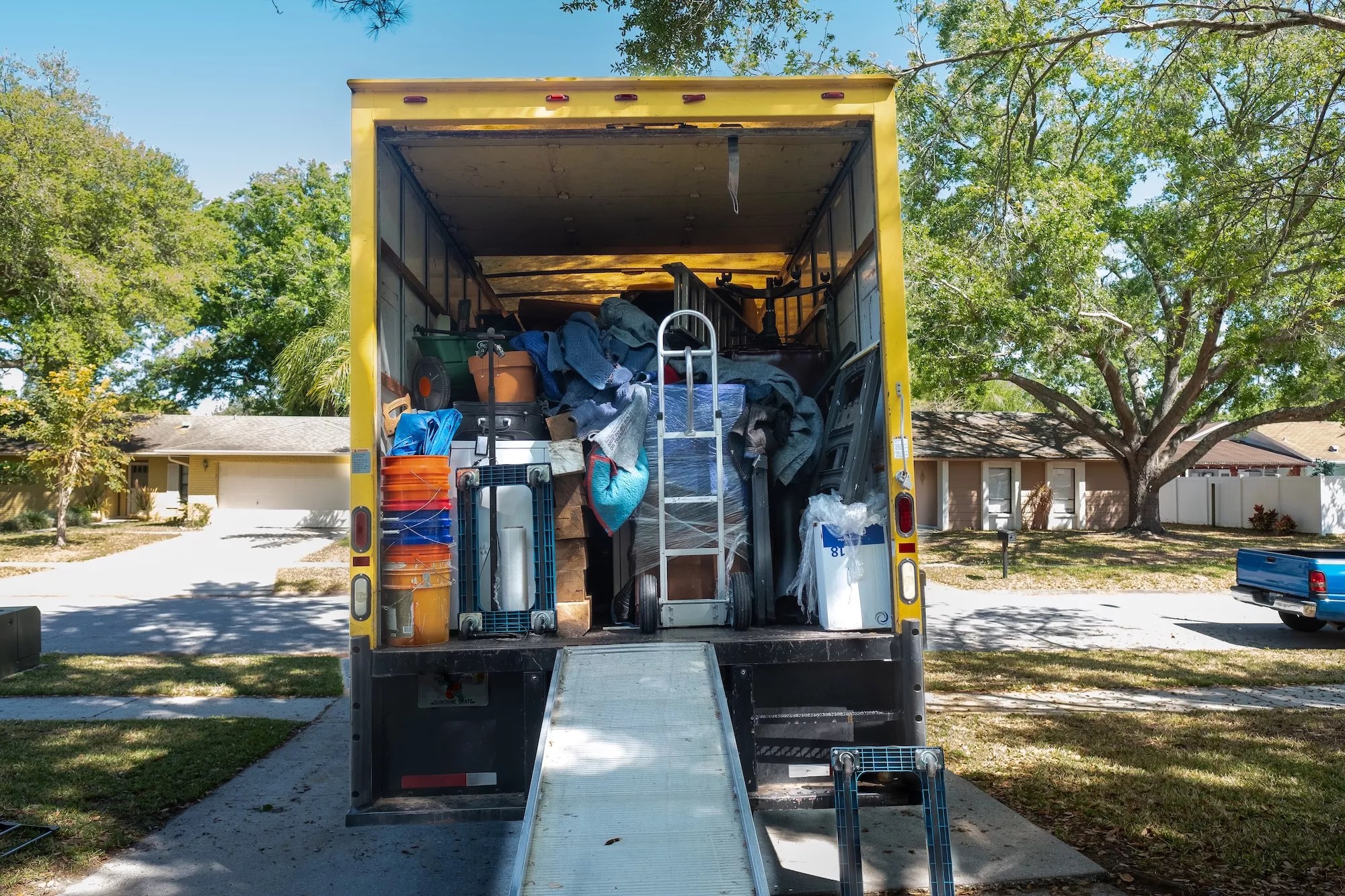 Belongings from a house loaded into a moving van, viewed from the back of the truck, including ramp and dolly.