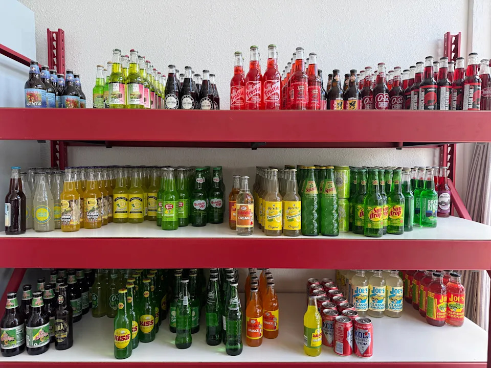 Assorted sodas on a tiered red shelf.