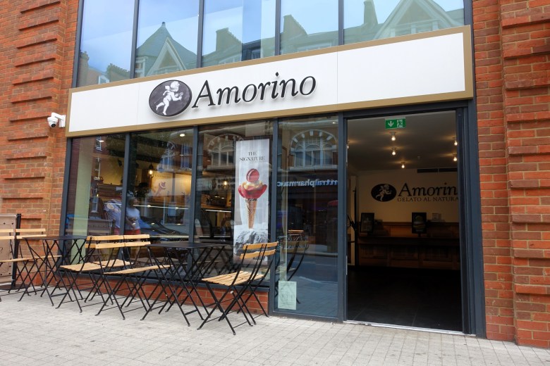 Exterior of an Amorino Gelato with tables and chairs outside and a poster of its signature rose-shaped gelato cone
