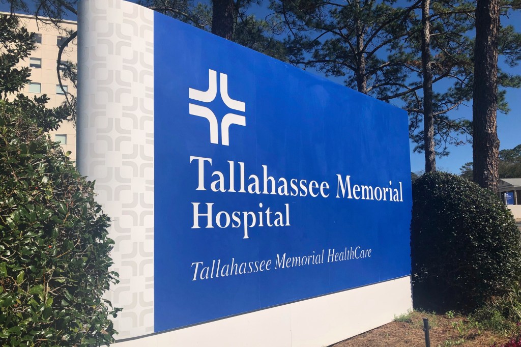 A sign for Tallahassee Memorial Hospital with a building and trees in the background.