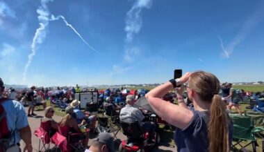Behind a crowd of spectators, a woman records an air show taking place at the Sun 'n Fun Aerospace Expo in April 2024. (Spectrum News/Tim Kania)