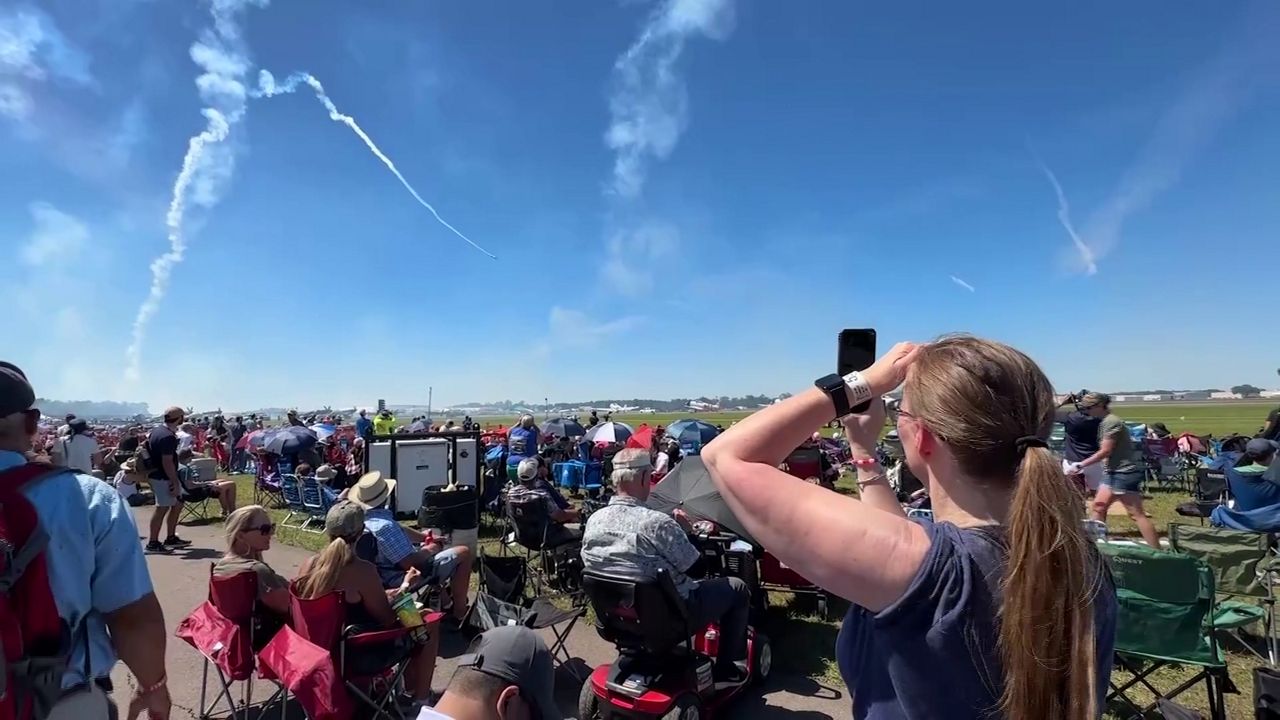Behind a crowd of spectators, a woman records an air show taking place at the Sun 'n Fun Aerospace Expo in April 2024. (Spectrum News/Tim Kania)