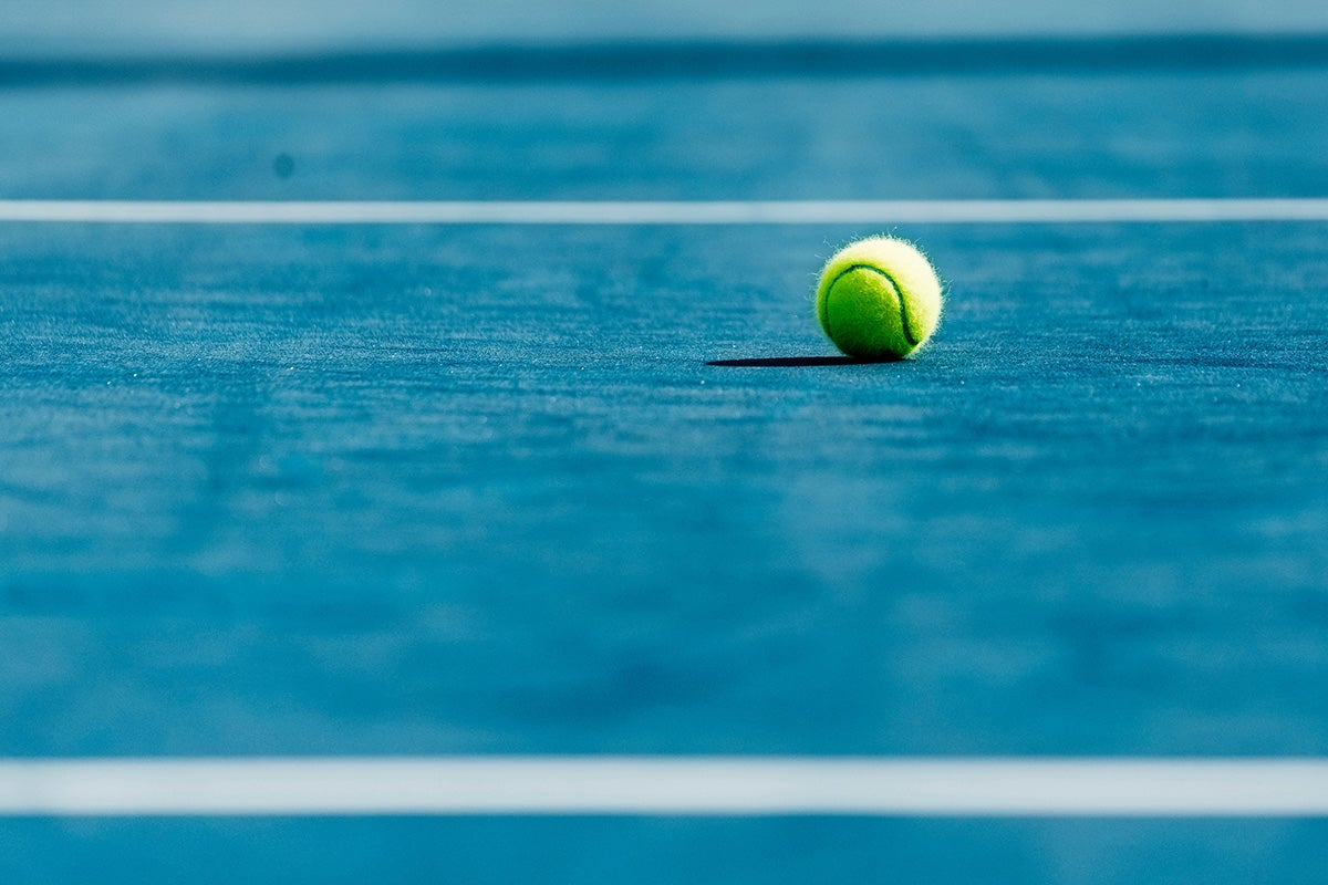 A lone tennis ball on a blue court with white lines
