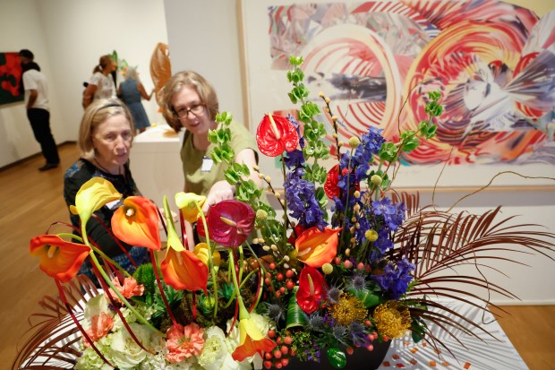 Windermere Garden Club member Amy Jain, left, and her daughter, Angela Withers, discuss the floral arrangement by Haley Johnson, inspired by the swirling patterns of the artwork The Stowaway Peers Out at the Speed of Light by James Rosenquist, displayed on the wall behind them during Art in Bloom, the annual Council of 101 event and fundraiser, on Friday, April 10, 2026. (Rich Pope/Orlando Sentinel)
