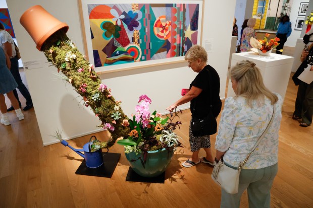 Mary Kay Pieski points out floral details to Cathy Adams on the arrangement by Heather Escobar and Laura Cosgrove, inspired by the artwork Dovetail by Beatriz Milhazes, on display on the wall during Art in Bloom at the Orlando Museum of Art on Friday, April 10, 2026, the annual Council of 101 event and fundraiser. (Rich Pope/Orlando Sentinel)