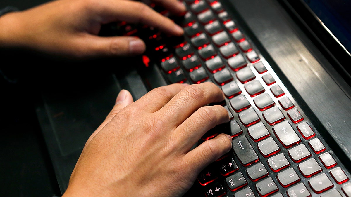 Scammer typing on a laptop keyboard.