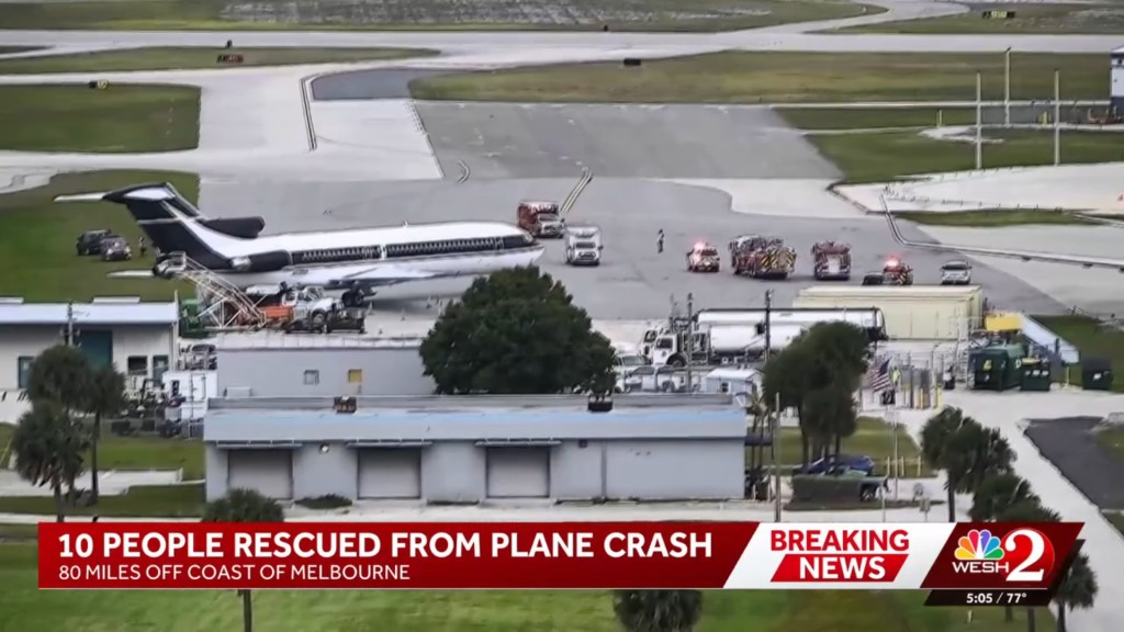 An airplane on the tarmac with emergency vehicles nearby, accompanied by a news banner reading "10 PEOPLE RESCUED FROM PLANE CRASH 80 MILES OFF COAST OF MELBOURNE".