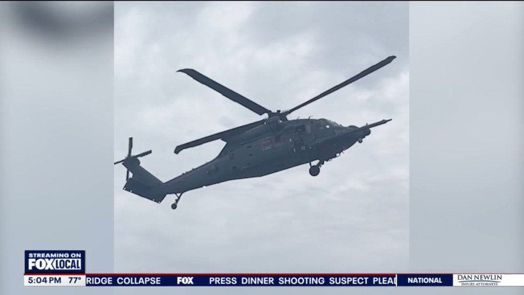 A dark gray helicopter flying against a cloudy sky.