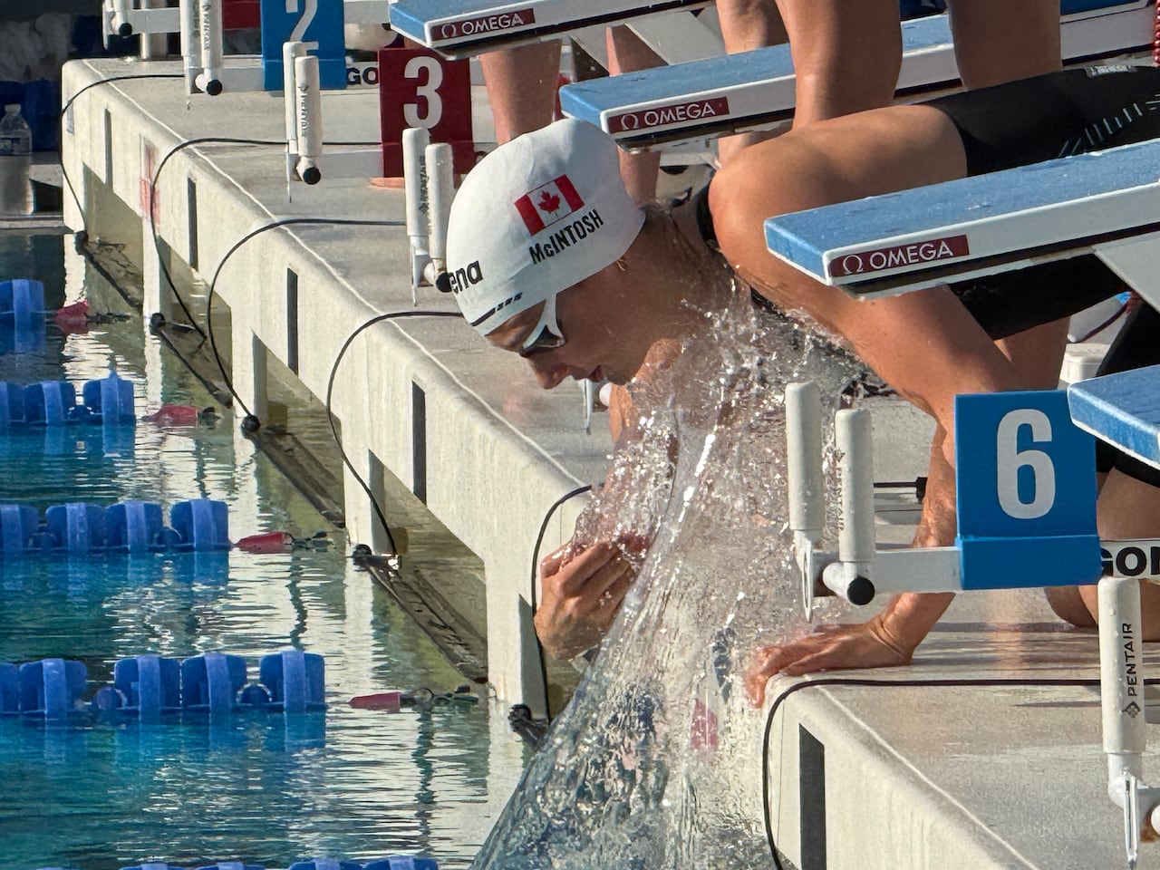 A female swimmer representing Canada splashes the water while crouching down near the edge of the pool.
