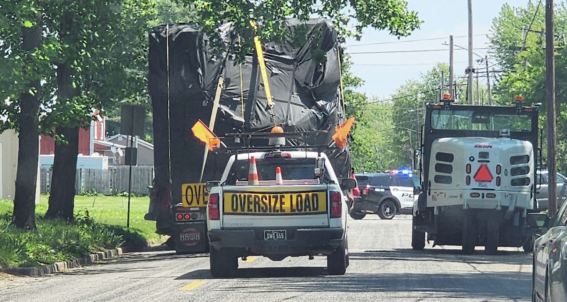 A Jacksonville police escort pauses at East State and Johnson streets as a tractor-trailer hauling an oversize load eases around a city street sweeper and under power lines. Police helped guide the truck's driver out of town Monday after overpasses along his route proved too low for the truck's load to pass under.