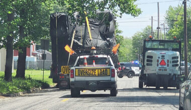 A Jacksonville police escort pauses at East State and Johnson streets as a tractor-trailer hauling an oversize load eases around a city street sweeper and under power lines. Police helped guide the truck's driver out of town Monday after overpasses along his route proved too low for the truck's load to pass under.
